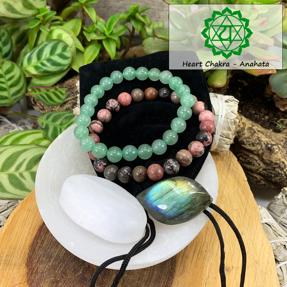 Green aventurine and rhodonite mala bracelets on a black velvet pouch with a white selenite ellipse and a labradorite cabochon, beside a Heart Chakra Anahata symbol