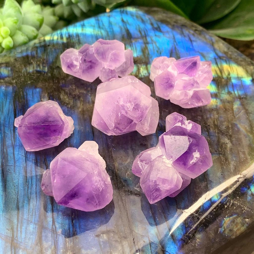 Seven amethyst fairy clusters in different shapes resting on a polished labradorite slab