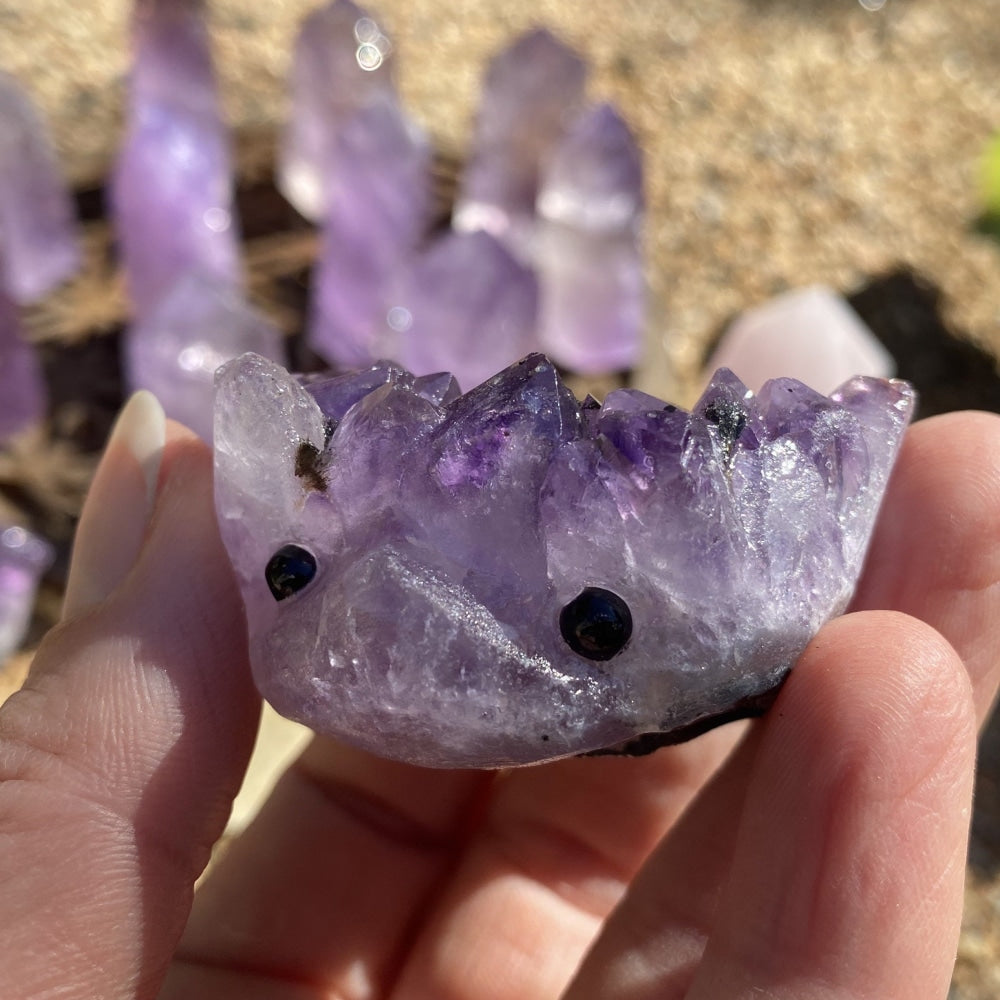 Amethyst hedgehog with crystal-point quills and two black bead eyes, held between fingertips