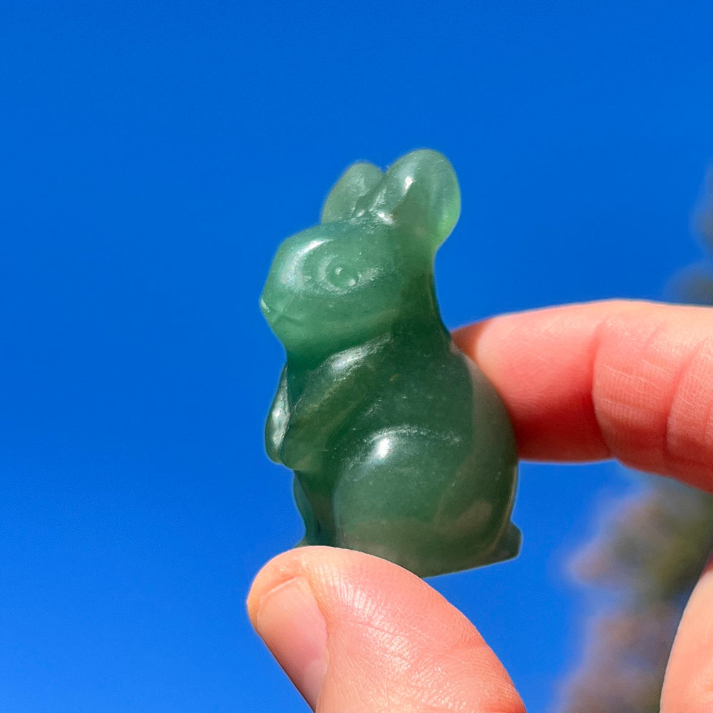 A small carved green rabbit held between a thumb and fingertip against a blue sky
