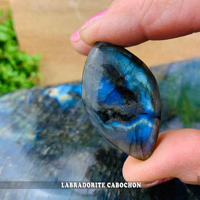 A domed labradorite cabochon held between finger and thumb, showing a band of blue