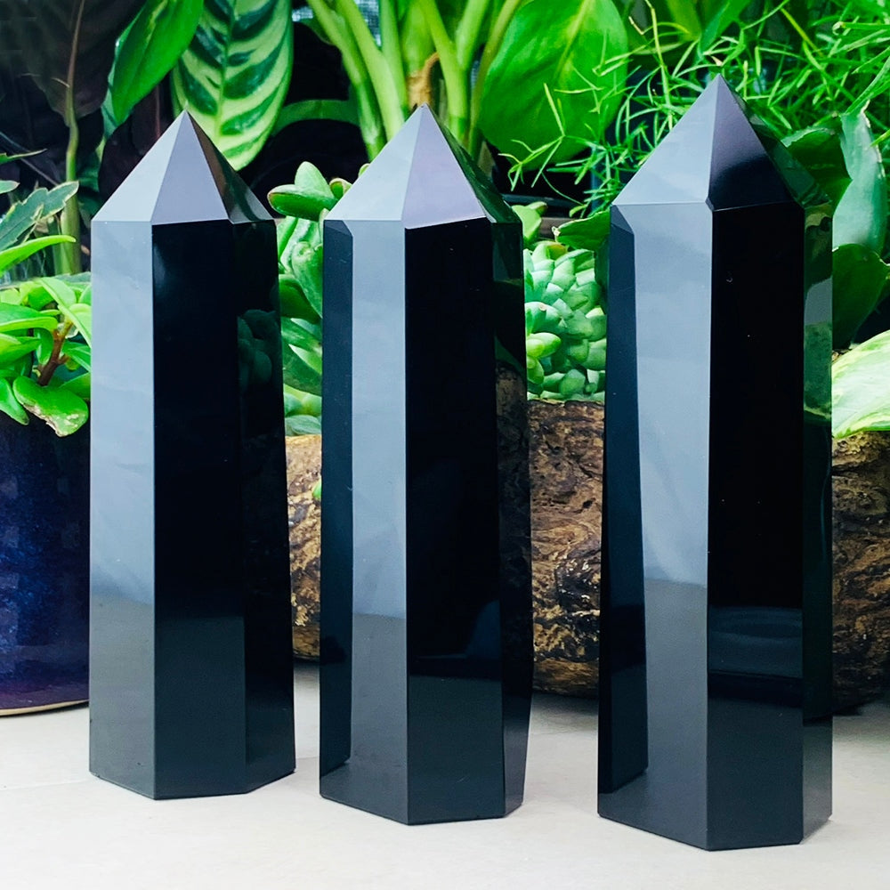 Three polished black obsidian generator towers standing in front of green plants, their faces reflecting the leaves